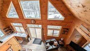 Ein gemütliches Cabin-Interieur mit Essbereich, einer Couch, einem Kamin und mehreren Fenstern mit Blick auf eine verschneite Landschaft.