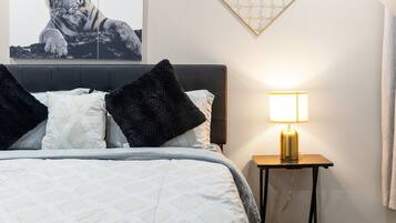 Ett sovrum med en säng, ett nattduksbord, en lampa, en tavla med ett tigermotiv och en geometrisk väggdekoration.