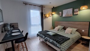A bedroom with a bed, a dining table with chairs, a small round table, and a window with curtains. - Studio Cosy le Natureavec Parking Fermé (Lourdes)