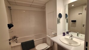 A bathroom with a bathtub, toilet, sink, and a large mirror. - Studio Cosy le Natureavec Parking Fermé (Lourdes)