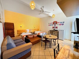 A hotel room with a sofa, two beds, a dining table, a ceiling fan, wall-mounted lights, a microwave, and a TV.