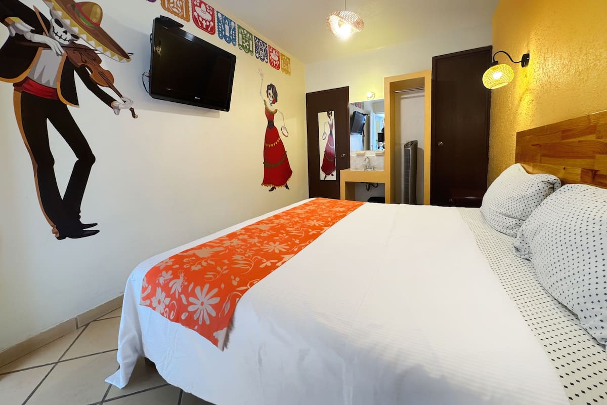 Habitación de hotel con cama, televisión, espejo y decoración cultural en la pared.