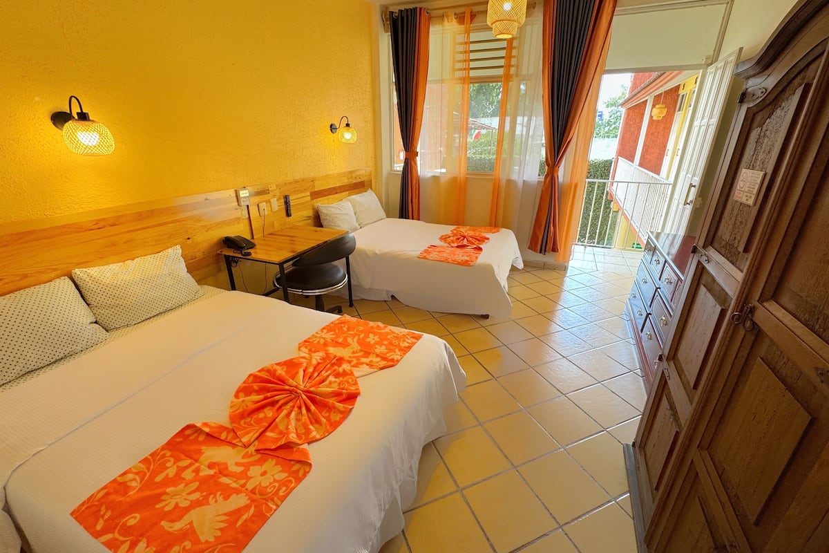 Habitación de hotel con dos camas, un escritorio pequeño y un balcón con cortinas.