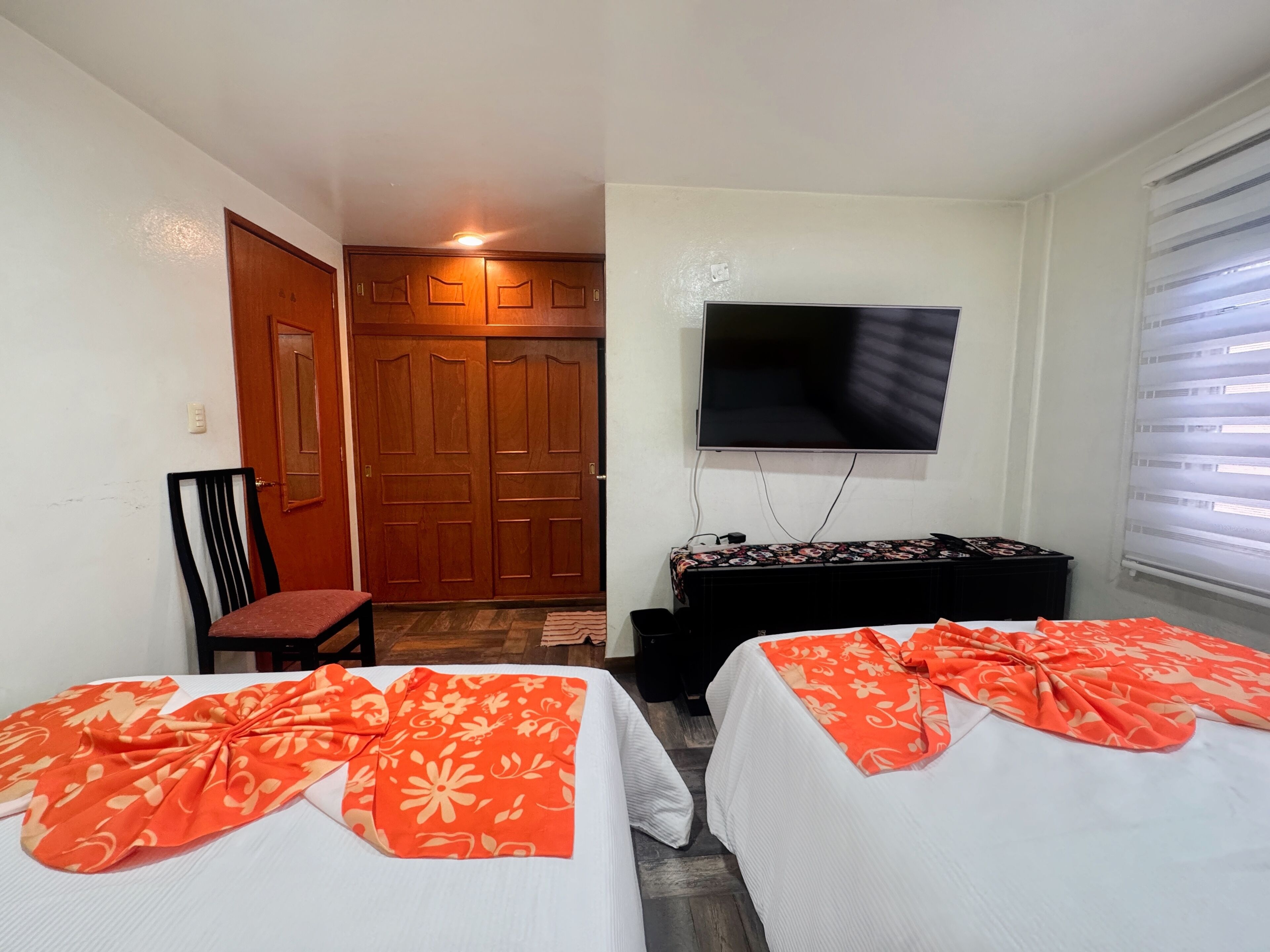 A hotel room with two beds, a TV, a wooden wardrobe, and a small table.