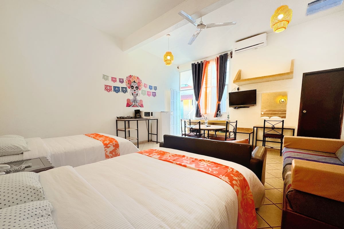 Habitación de hotel con dos camas, un escritorio, una silla, un televisor y un ventilador de techo.