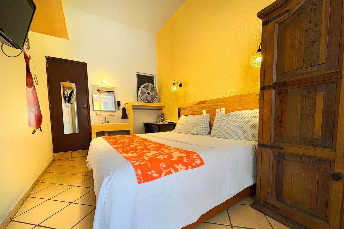 Una habitación de hotel con cama, armario de madera, baño con espejo y ventilador.