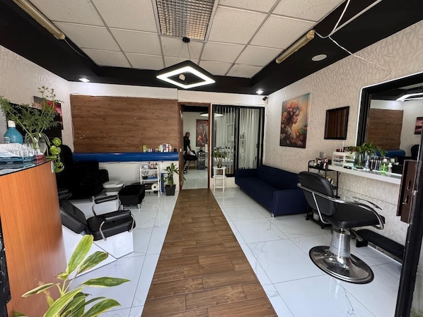 Ein Friseursalon mit einer Rezeption, zwei Frisierstühlen, einem blauen Sofa und einem Holzboden.
