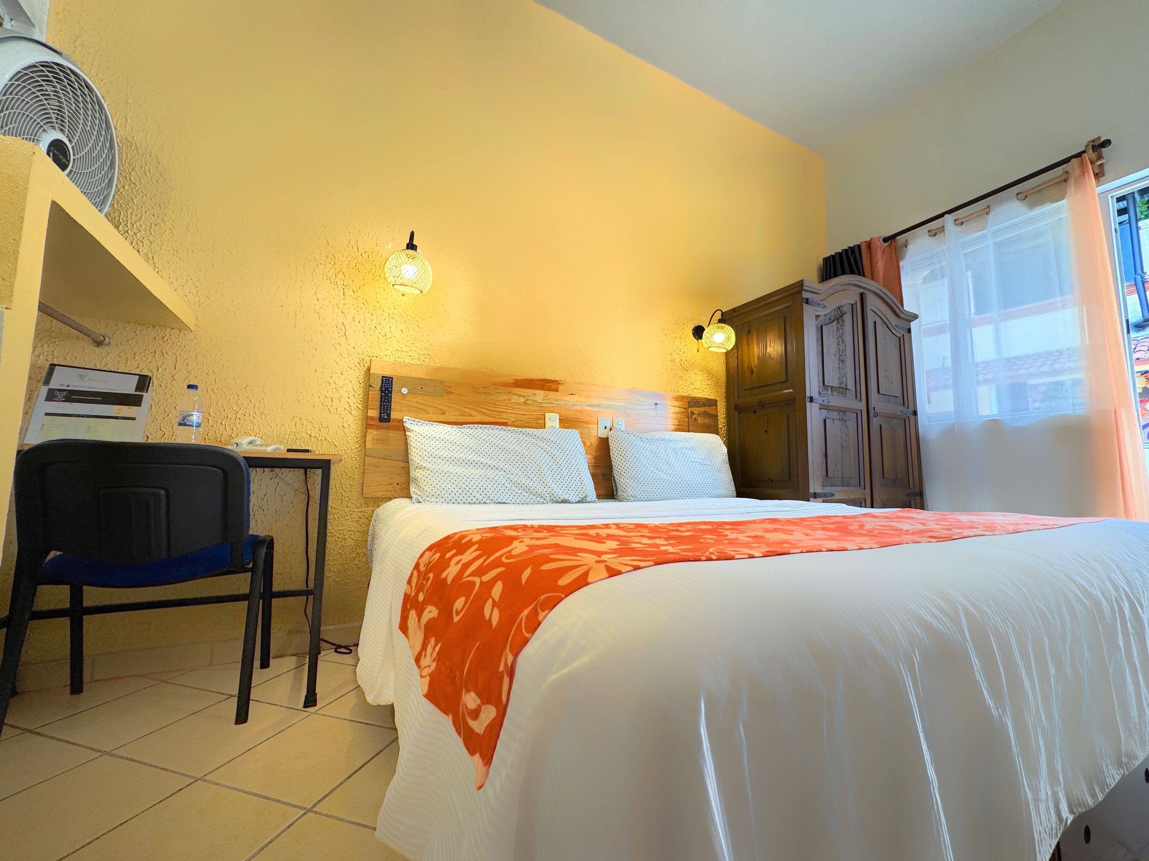 A hotel room with a bed, a desk, a chair, a wardrobe, and a window with curtains.