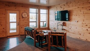 Una habitación acogedora con paredes y puerta de madera, un reloj, un televisor y una mesa con sillas.