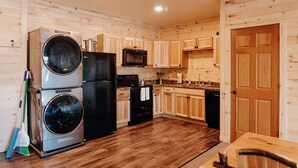 Cocina compacta con armarios de madera, microondas, refrigerador de dos puertas y lavadora.