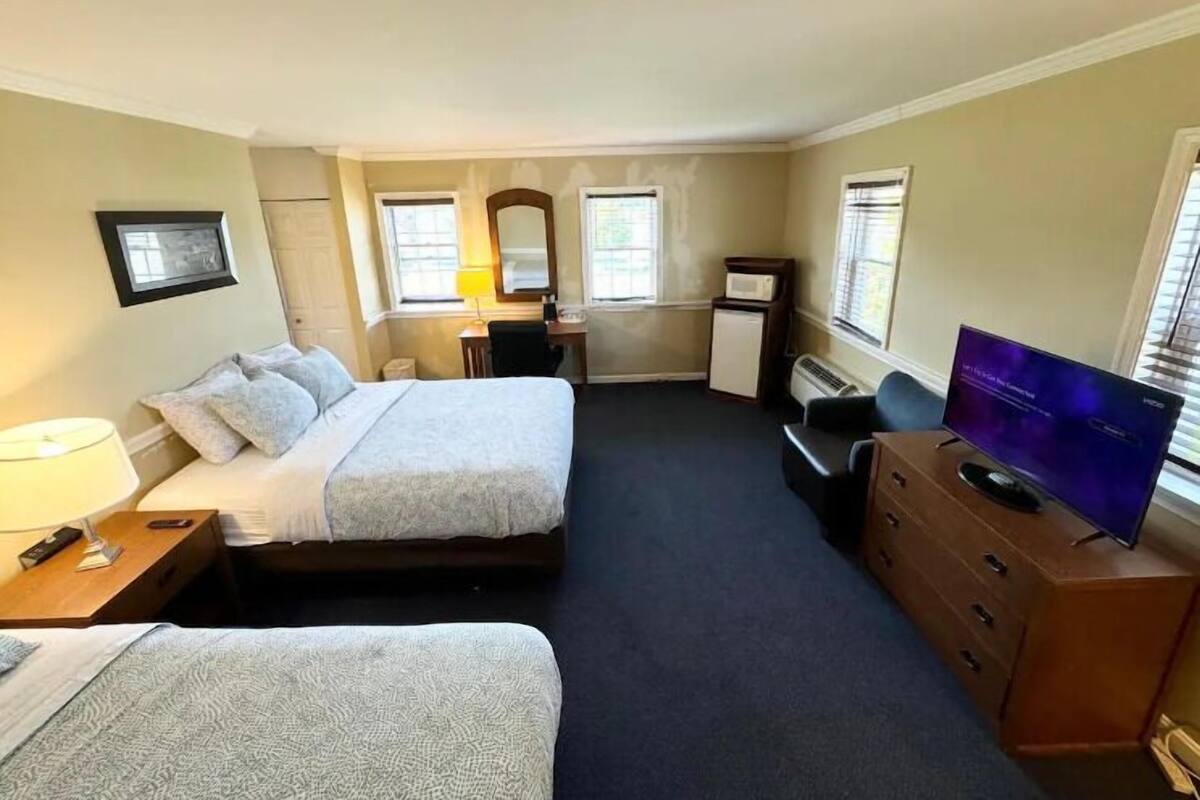A hotel room with two beds, a desk, a TV, and a dresser.