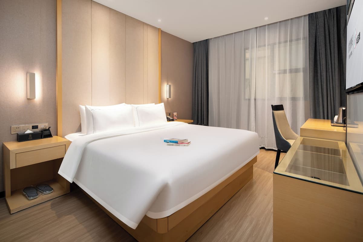 A modern hotel room with a large bed, bedside tables, a glass coffee table, and a view of the city.