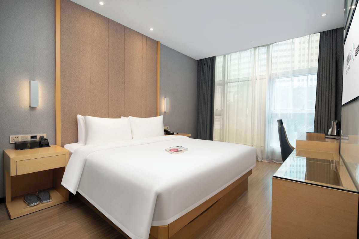 A modern hotel room with a large bed, bedside tables, a desk, and a large window.