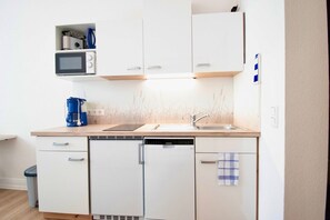 Uma cozinha compacta com armários brancos, micro-ondas, cafeteira e lava-louças.