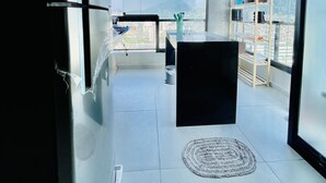 A modern interior with a large window, a black sofa, a coffee table, and a wooden shelf with items. - Apartamento Novo A 600 Metros DA Praia (Balneario Cidade Atlantica Guarujá)
