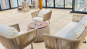 A rooftop terrace with wicker furniture, a round table, and a city view. - Apartamento Novo A 600 Metros DA Praia (Balneario Cidade Atlantica Guarujá)