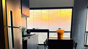 A modern kitchen with a large window, a dining table, and a refrigerator. - Apartamento Novo A 600 Metros DA Praia (Balneario Cidade Atlantica Guarujá)