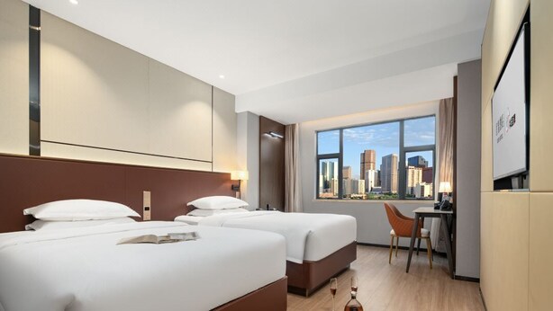 A hotel room with two beds, a desk, and a chair. There is a large window with a city view. - Yizhi Hotel Panyu Plaza Shiqiao Subway   (Guangzhou)