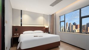 A modern hotel room with a large bed, a nightstand, a desk, and a view of a city skyline through large windows. - Yizhi Hotel Panyu Plaza Shiqiao Subway   (Guangzhou)