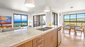 Een moderne keuken met een groot eiland, houten kasten en uitzicht op zee.
