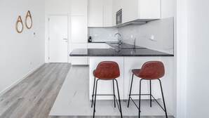 A modern kitchen with white cabinetry, a black countertop, and two red bar stools. - GuestReady - A lovely vacation in Matosinhos (Matosinhos)