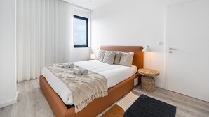 A modern bedroom with a large bed, a bedside lamp, a small side table, and a view of the city through a window. - GuestReady - A lovely vacation in Matosinhos (Matosinhos)