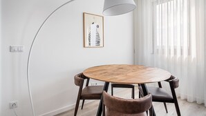 A dining area with a round wooden table, two brown leather chairs, a modern pendant lamp, and a framed abstract artwork on the wall. - GuestReady - A lovely vacation in Matosinhos (Matosinhos)