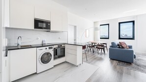 A modern kitchen with a washing machine, a dining area with a table and chairs, and a living room with a sofa and a large window. - GuestReady - A lovely vacation in Matosinhos (Matosinhos)