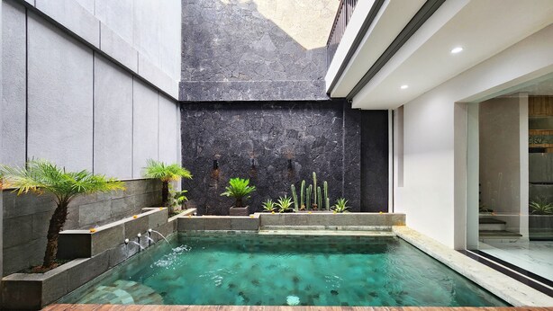 A modern indoor pool with clear water, surrounded by stone walls and various plants. - Villa Rumpi Seminyak by Nagisa Bali (Legian)