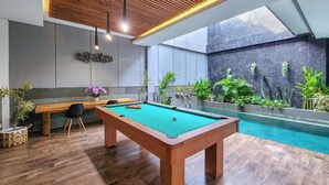 A pool table in a modern indoor setting with wooden flooring, a bench, and potted plants. - Villa Rumpi Seminyak by Nagisa Bali (Legian)