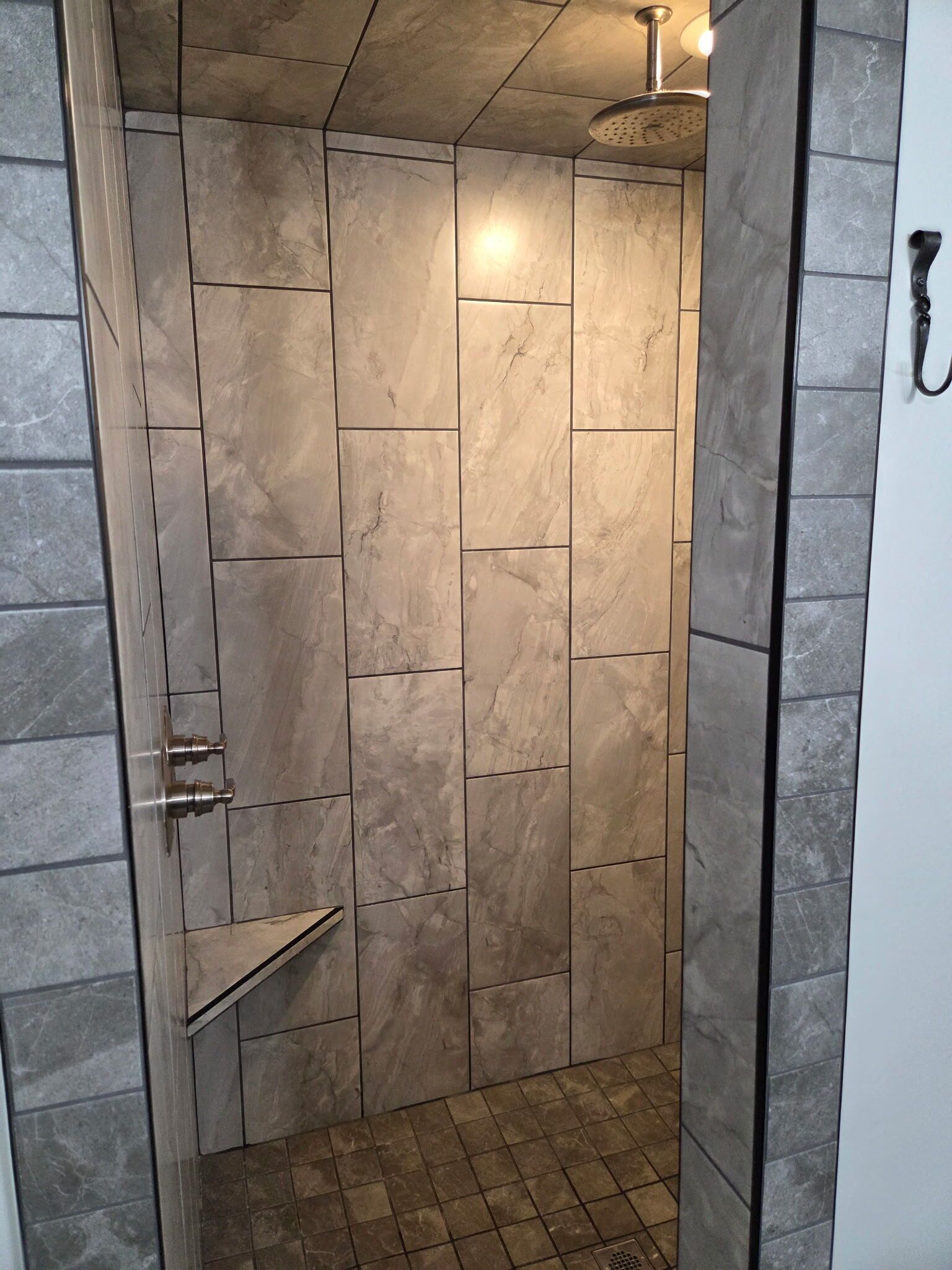A shower with a handheld showerhead, a shelf, and a door with a handle.