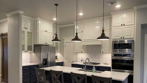 A modern kitchen with white cabinetry, a central island with bar stools, stainless steel appliances, and pendant lighting.