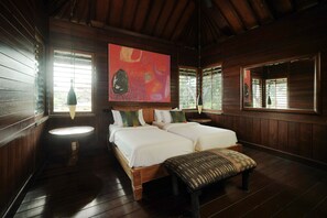 A wooden room with two beds, a round table, and a large abstract painting on the wall.