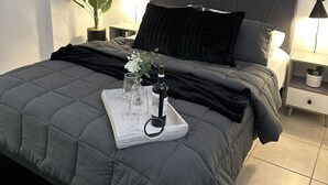 Ein modernes Schlafzimmer mit einem großen Bett, einem Nachttisch, einer Topfpflanze und abstrakter Wandkunst.