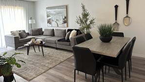 Ein modernes Wohnzimmer mit einem grauen Ecksofa, einem runden Esstisch mit schwarzen Stühlen, einem Couchtisch und einem großen Gemälde an der Wand.