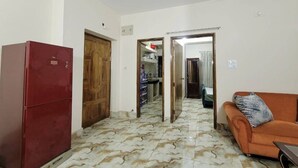 A room with a tiled floor, a red refrigerator, a wooden door, and an orange sofa. - Lovely two bed flats, by Dhaka Shahjalal Airport (Dhaka)