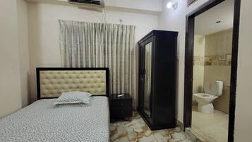 A bedroom with a bed, a wardrobe, an air conditioner, and a bathroom visible through an open door.