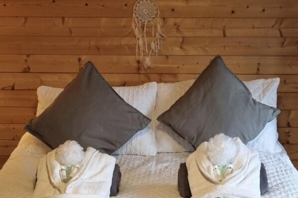 A wooden cabin room with a bed featuring two pillows and two towels.