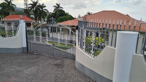 A gated compound with a paved entrance, a covered outdoor area with a red roof, and a white building with a balcony. - Beautiful 2-Bed Apartment in Montego Bay (Montego Bay)
