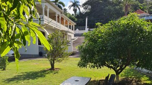 A grassy outdoor area with a picnic table and chairs, surrounded by trees and a building with a balcony. - Beautiful 2-Bed Apartment in Montego Bay (Montego Bay)