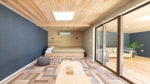 Une chambre moderne avec un plafond en bois, un lit, un petit coin salon et une grande porte-fenêtre coulissante donnant sur un espace extérieur.