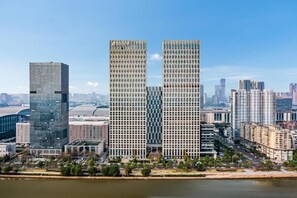 A high-rise building with a grid-like facade, situated near a body of water with a river in the foreground. - eStay Residence - Poly World Trade Center Guangzhou (Guangzhou)
