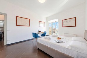 A modern hotel room with a large bed, a dining area with a table and chairs, and framed artwork on the walls.