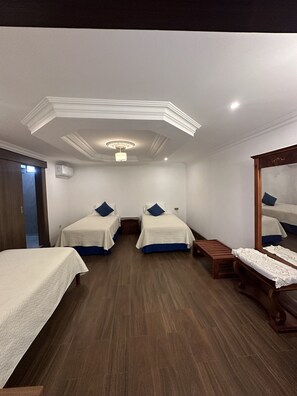 A hotel room with two beds, a wooden bench, a mirror, and a ceiling light.