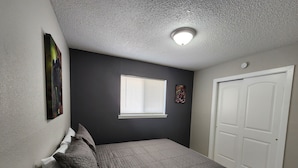 Une chambre à coucher avec un lit, une fenêtre, une porte et un luminaire au plafond.