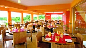 A restaurant with multiple tables and chairs, large windows, and a bright interior. - Nazimgarh Garden Resort (Sylhet)