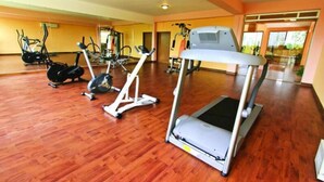 A gym with various cardio machines, wooden flooring, and a large mirror. - Nazimgarh Garden Resort (Sylhet)