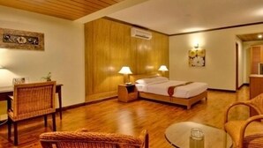 A hotel room with a wooden floor, a bed with white linens, two bedside lamps, a small table with a glass, and a chair. - Nazimgarh Garden Resort (Sylhet)