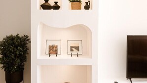 A modern living room with built-in shelving displaying decorative items, a television, and a potted plant. - Villa located in "Douro Verde" with outdoor pool, 5 minutes from the Douro River (Paços de Gaiolo)