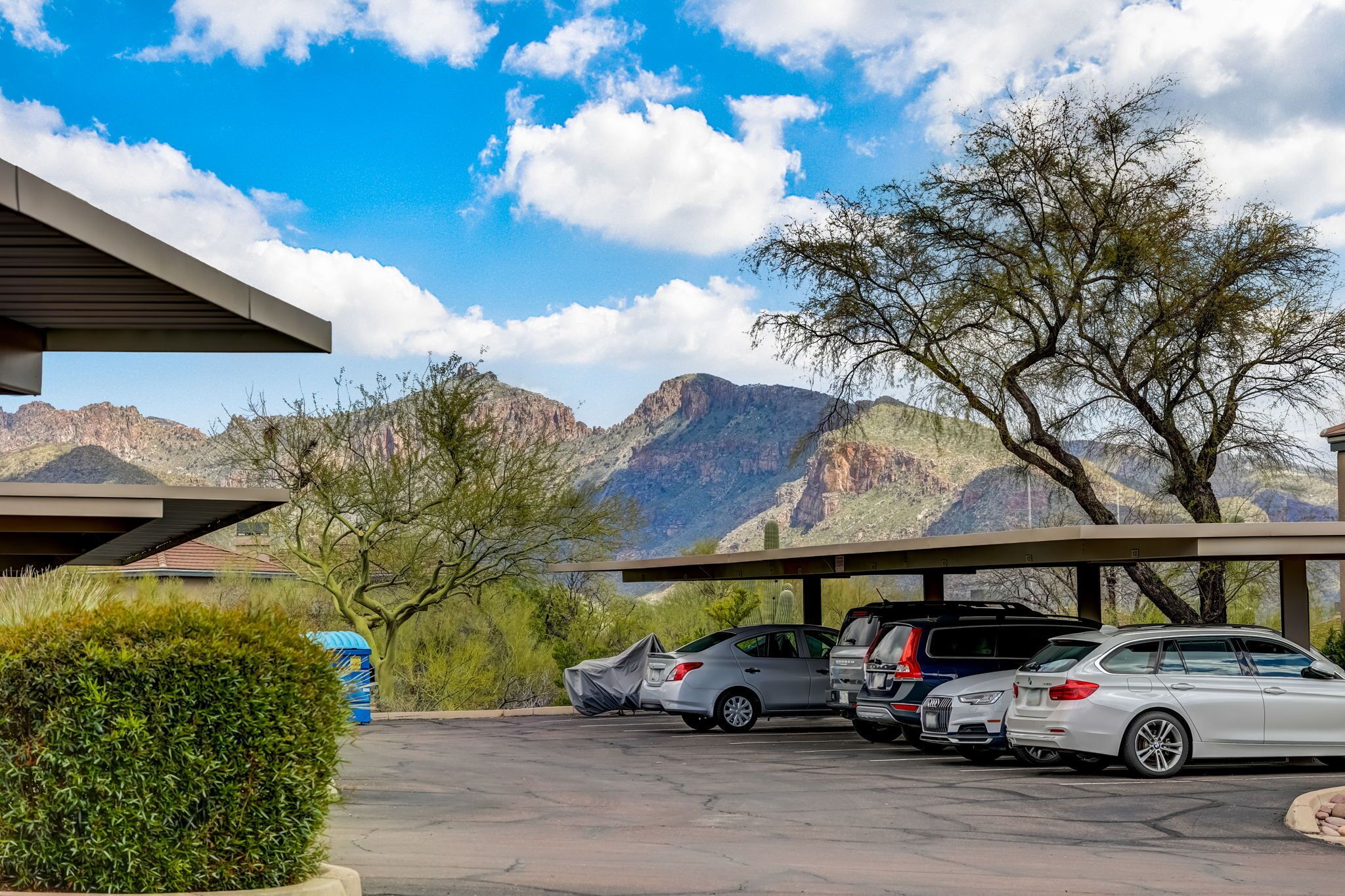 A parking area with several cars, a covered structure, and a mountainous landscape in the background.